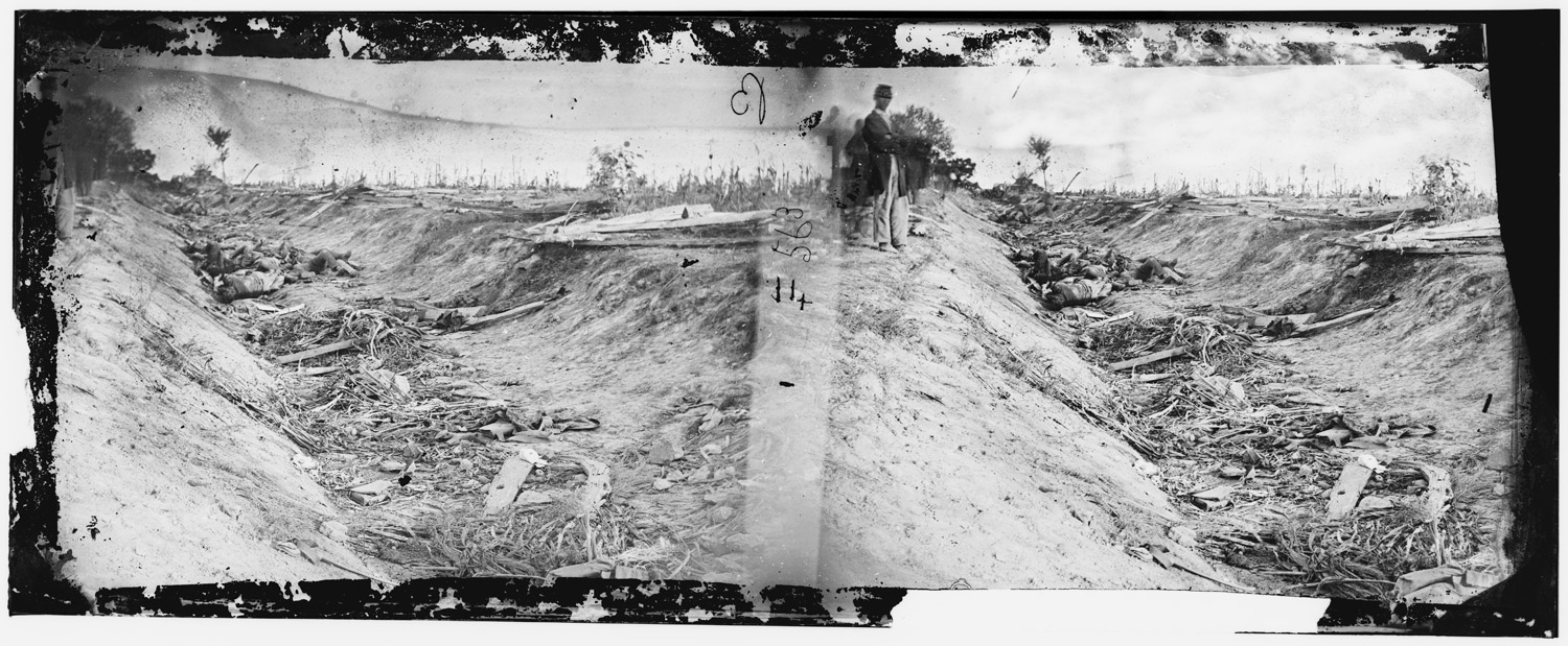 A Union soldier poses near a trench with dead Confederate soldiers after the Battle of Antietam, September 1862.