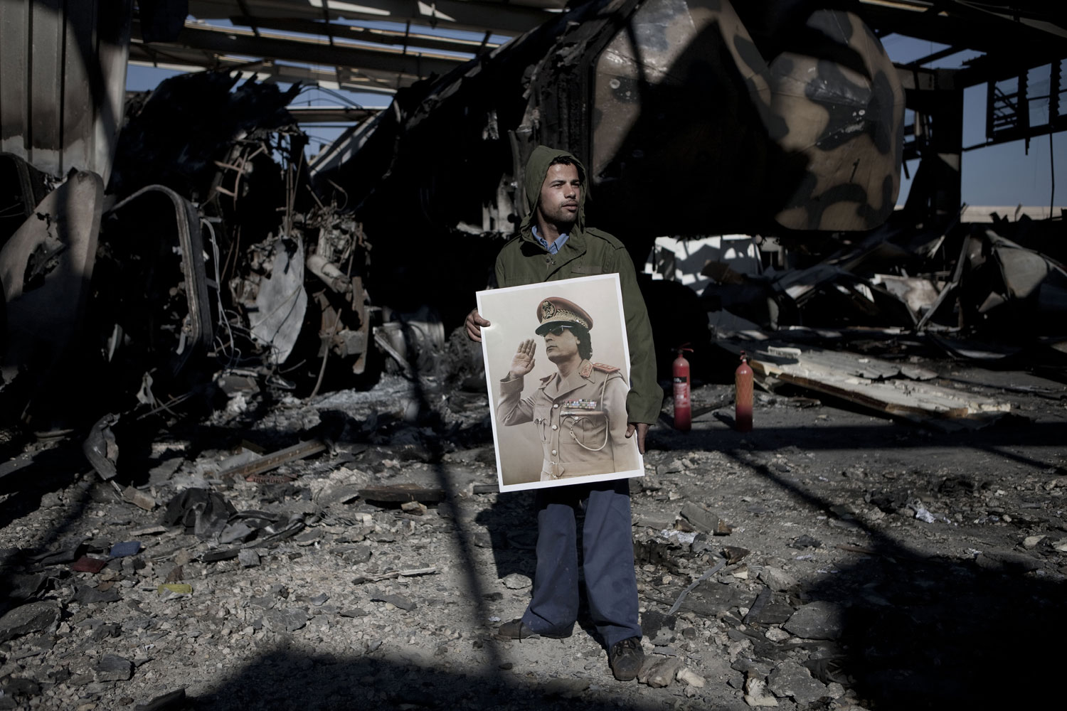 A Gaddafi supporter holds a portrait of the Libyan leader for the media during a tour of a building struck by missiles, March 22, 2011.