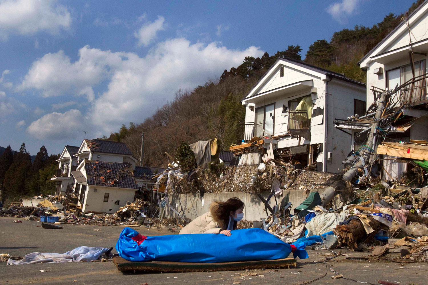 Tayo Kitamura, 40, kneels in the street to caress and talk to the wrapped body of her mother Kuniko Kitamura, 69, after Japanese firemen discovered the dead woman inside the ruins of her home in Onagawa, northeastern Japan Saturday, March 19, 2011.