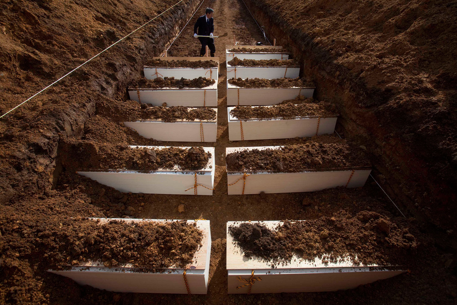 A Japanese funeral parlor worker shovels dirt on to coffins containing victims of the march 11 earthquake and tsunami during a mass funeral in Yamamoto, northeastern Japan Saturday, March 26, 2011.