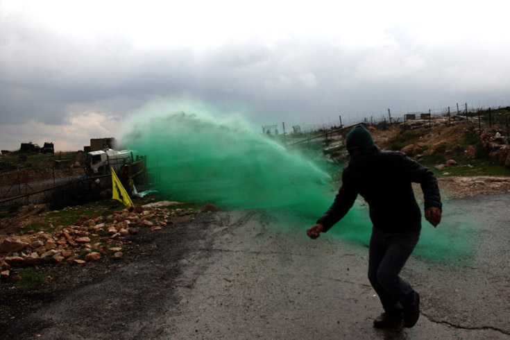 A Palestinian protester runs as colored water is sprayed by the Israeli army from a water cannon during the weekly demonstration against Israel's separation barrier in the village of Bilin, near the West Bank city of Ramallah on March 11, 2011.
