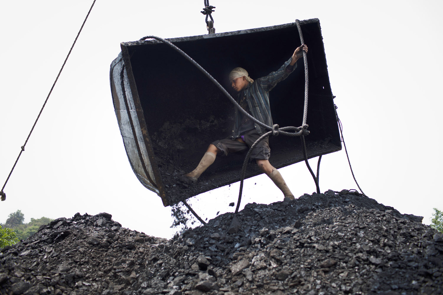 Fourteen-year-old Chhai Lyngdoh, kicks out the coal from a container, as it is emptied onto a heap, after being craned out of a 300ft deep mine shaft.