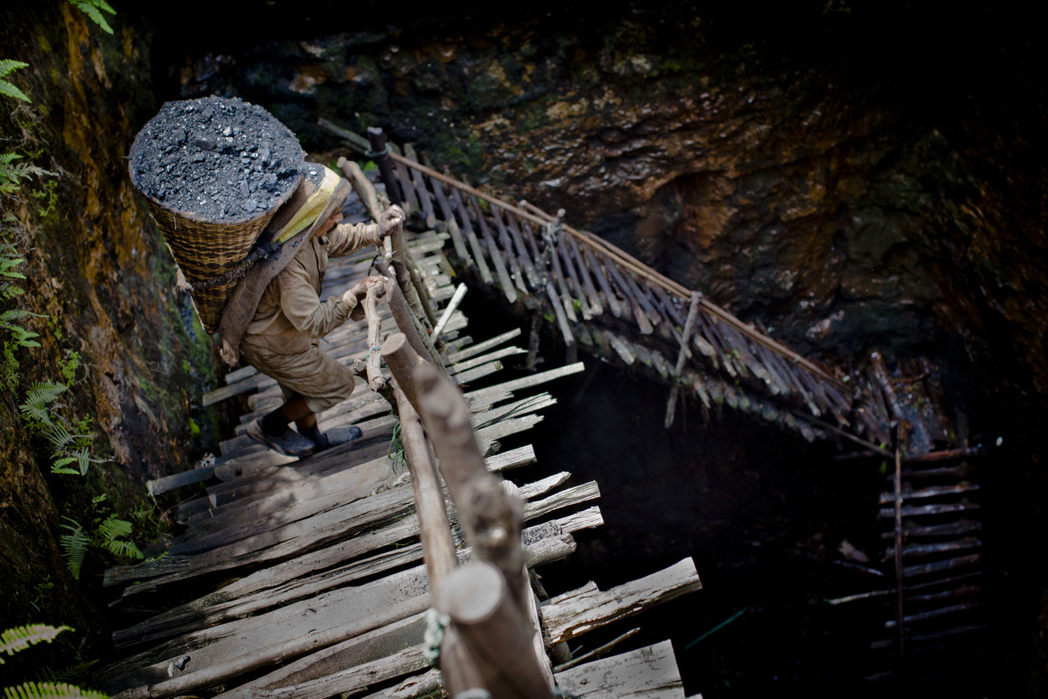Prabhat Sinha, from Assam, carries a load of coal weighing 60kg's, supported by a head-strap, as he ascends the staircase of a coal mine near the village of Khliehriat, in the district of Jaintia Hills, India.  miners descend to great depths on slippery, rickety wooden ladders. Children and adults squeeze into rat hole like tunnels in thousands of privately owned and unregulated mines, extracting coal with their hands or primitive tools and no safety equipment.
