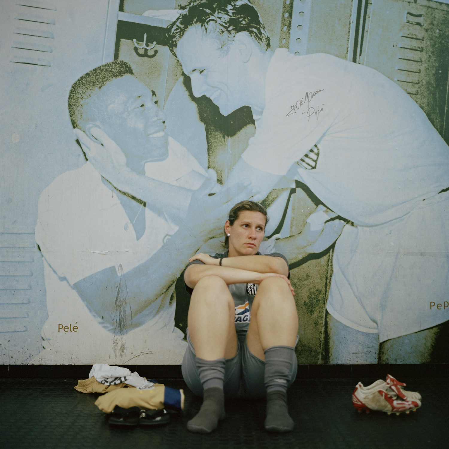 Santos goalkeeper Mayla, sits on the floor in front of a mural photograph of Santos FC men's legends, Pelé and Pepe, in the Estádio Vila Belmiro locker room.  Santos FC is known all over the world as the club where Pelé, the king of futebol, started his career at the age of 15. (December 3, 2010)