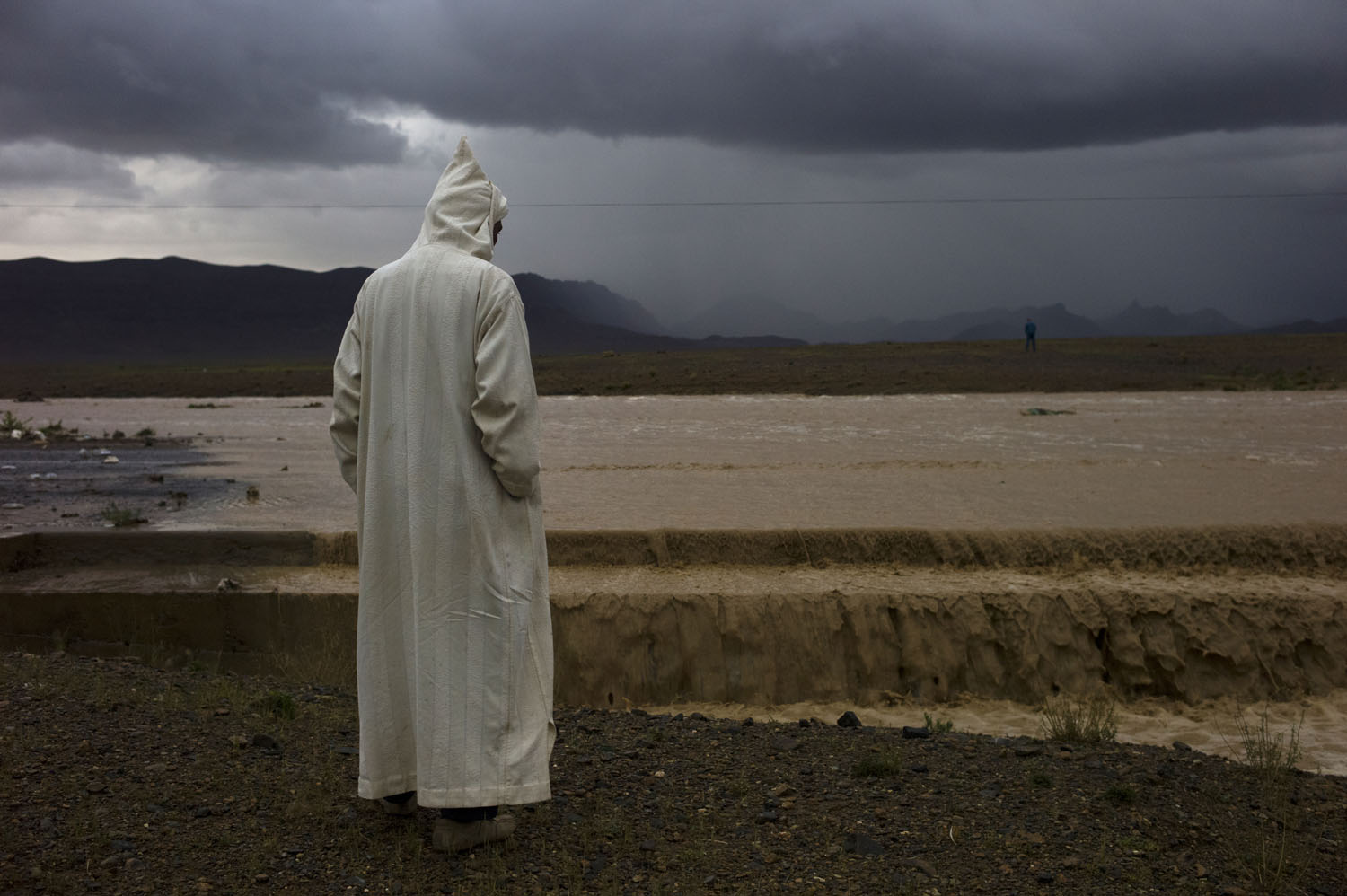 Morocco, 2011. 
                              A passenger of a bus waits while a flash flood takes out the road ahead of them near the northern edge of the Sahara desert in present-day Morocco
