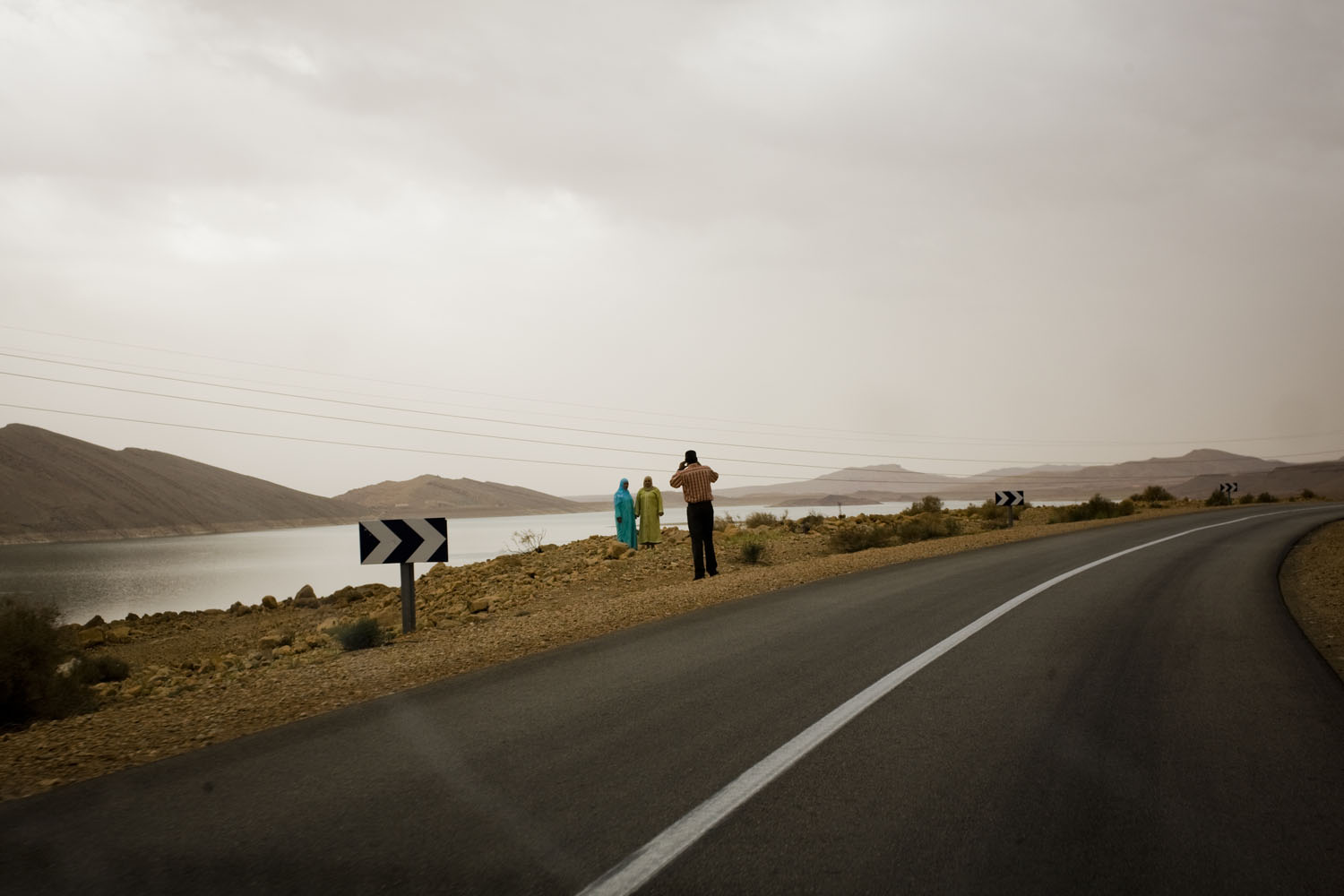 Morocco, 2011. 
                              A man takes a photograph of two women at the side of the road near the Algerian border.