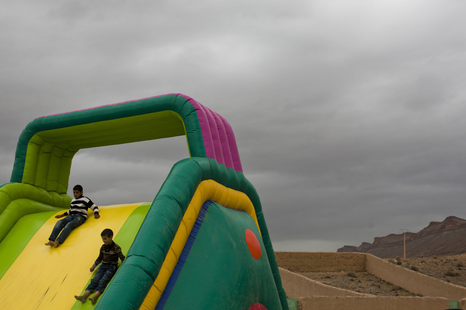 Morocco, 2011. 
                              Children play on a bouncy castle during a festival as a storm rolls in near the northern edge of the Sahara desert in present day Morocco.