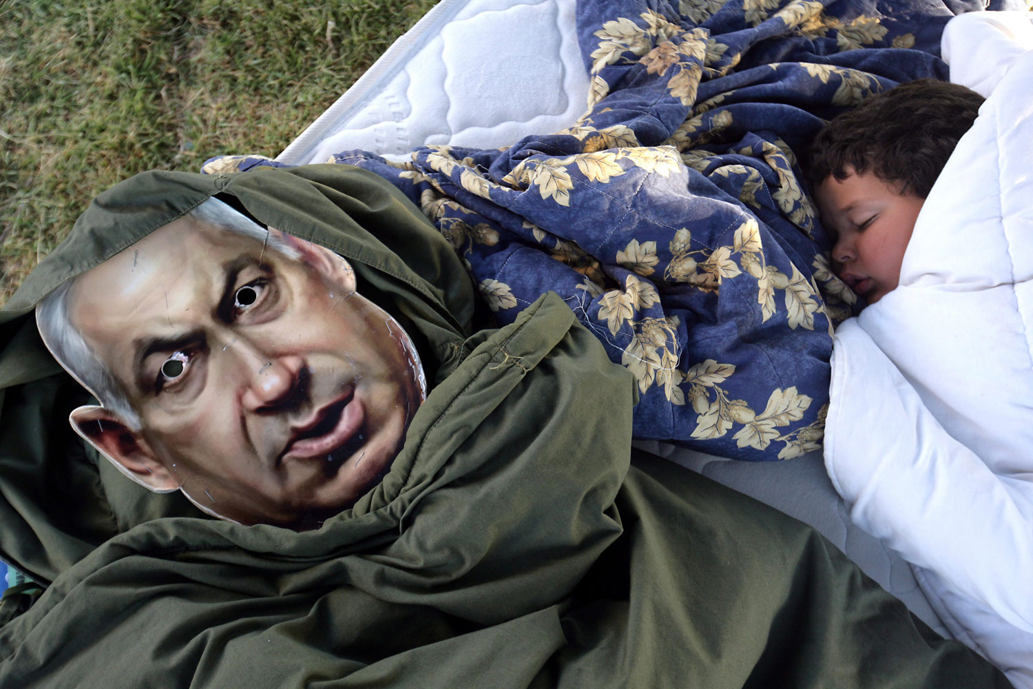 August 8, 2011. An Israeli child sleeps next to a picture of Israel Prime Minister Benjamin Netanyahu in a sleeping bag in a 'tent city' set up in a small central Jerusalem park, Israel. Israel's parliament passed a housing bill  aimed at alleviating the country's shortage of homes by cutting red tape to speed up the approval of building projects. But critics vowed to step up their protests after accusing the bill of failing to promote affordable housing. Leaders of the protest movement have also called for another mass rally to take place in Tel Aviv this weekend. Some 300,000 people demonstrated in major Israeli cities over the weekend, protesting the country's high cost of living.