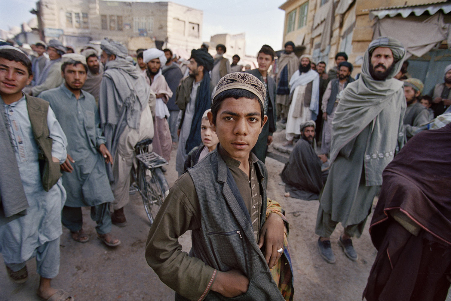 Local residents and Taliban gaze at a group of foreign journalists crossing through a central market following ten days of US airstrikes on city of Kandahar. November, 2001