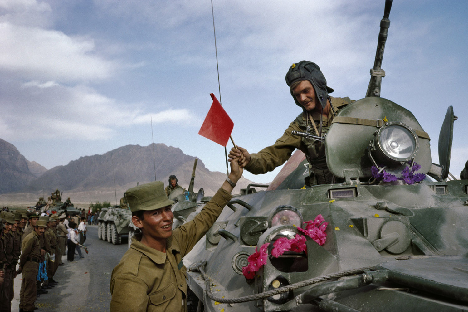 An Afghan army soldier hands a Soviet flag in solidarity to a departing soldier on the first day of the Soviet army's withdrawal from Afghanistan. May, 1988