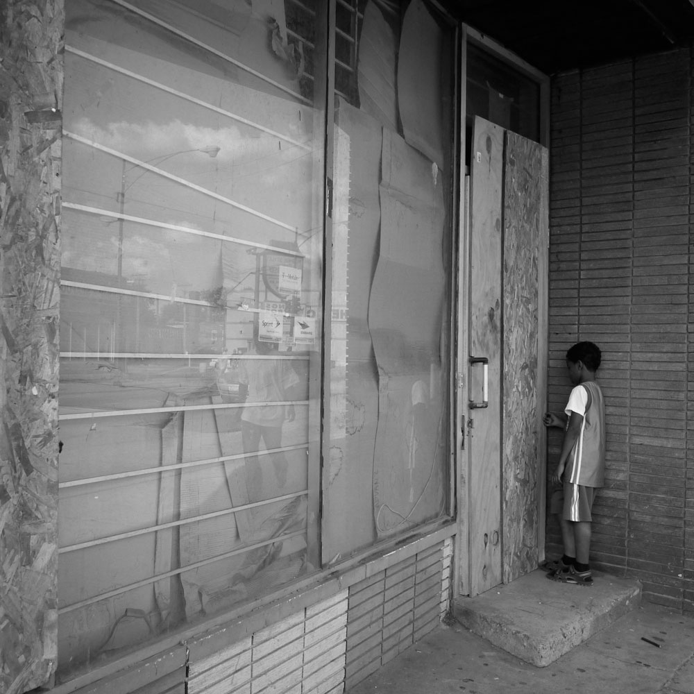 A child toys with the door of a boarded-up building in Auburn Gresham. Blight is a common visual reminder of the city’s economic neglect.