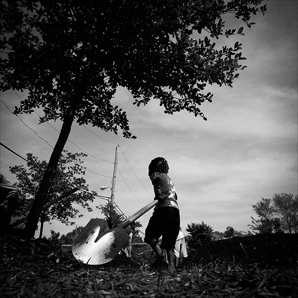 Two feet shorter than her shovel’s handle, a young child helps the organization WeFarm America install a community garden at SOS Chidren’s Village.