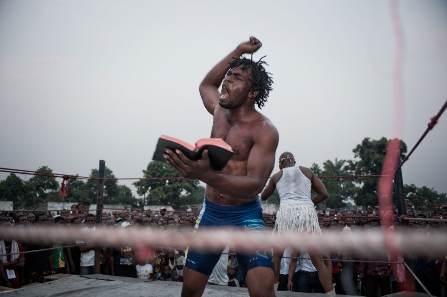 During a fetish match in Matete, the wrestler Tyson falls into a trance and starts to read the bible after being bewitched by his opponent, Alleluia, who stands, in white, with his back to the camera.