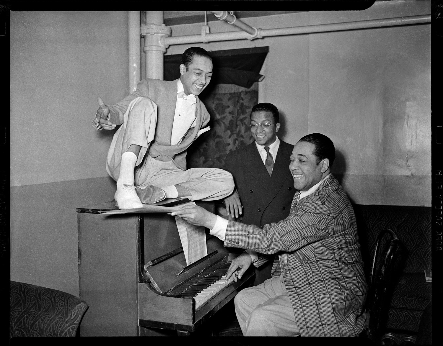 Duke Ellington at a piano with dancer Honey Coles and Billy Strayhorn looking on, in the Stanley Theatre, 1942-1943.