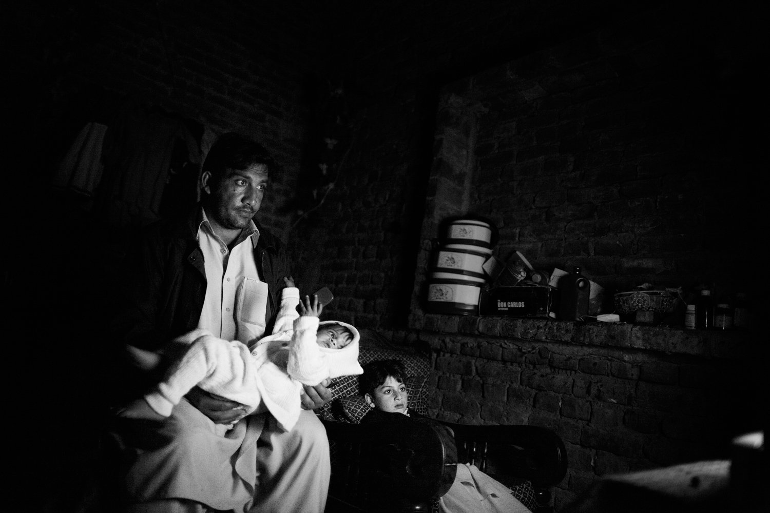 Pakistan, Swat Valley, Alligrama, March 2011. A Lashkar member, Ameer Zaib, watching TV in his bedroom with his children and trying to soothe his baby girl Gull Sangay to sleep. His young son Zaraq Khan is also with them.