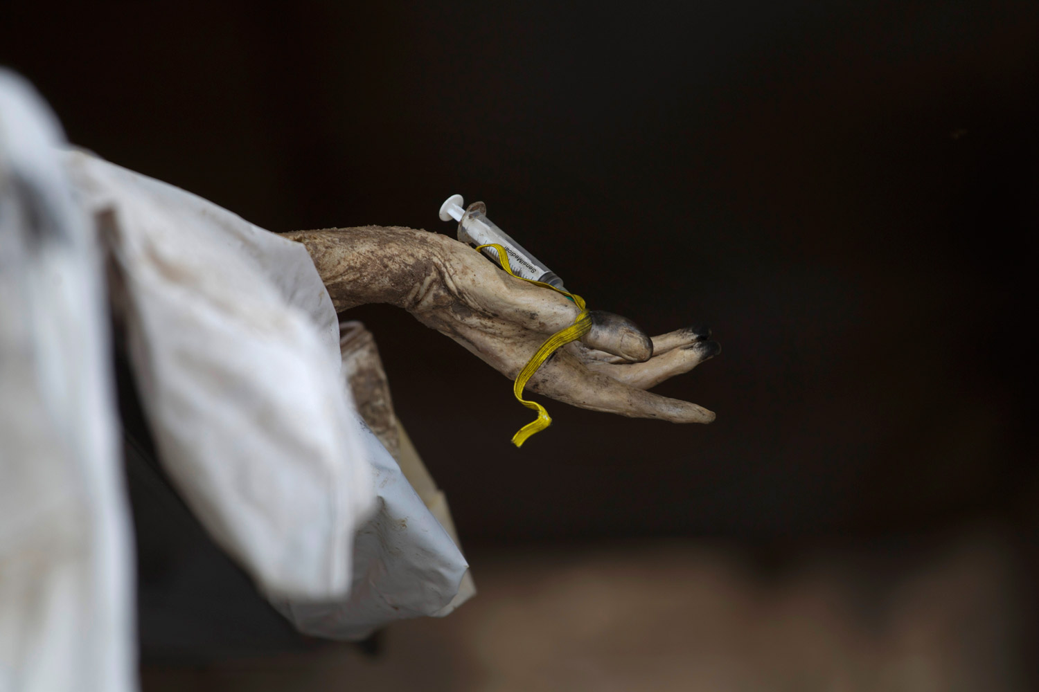 May 16, 2011. The hand of a corpse hangs from a bed with a syringe that is being used by forensic experts at a makeshift morgue inside a refrigerated container as they try to identify bodies found in mass clandestine graves in Durango, Mexico.