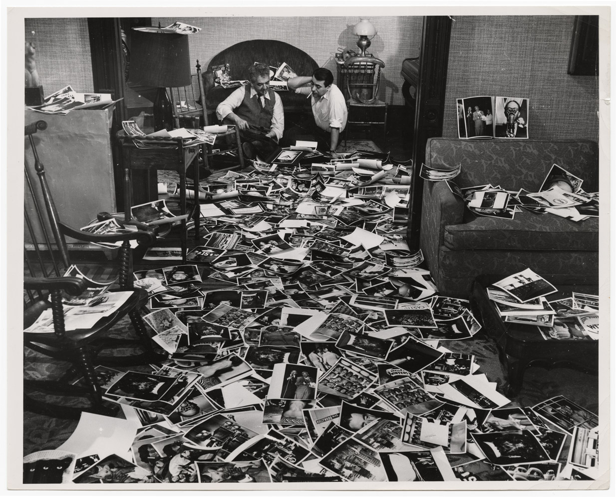 Weegee and his collaborator Mel Harris in Harris's home, which is carpeted by thousands of the photographer's prints for the Naked Hollywood book. ca.1952