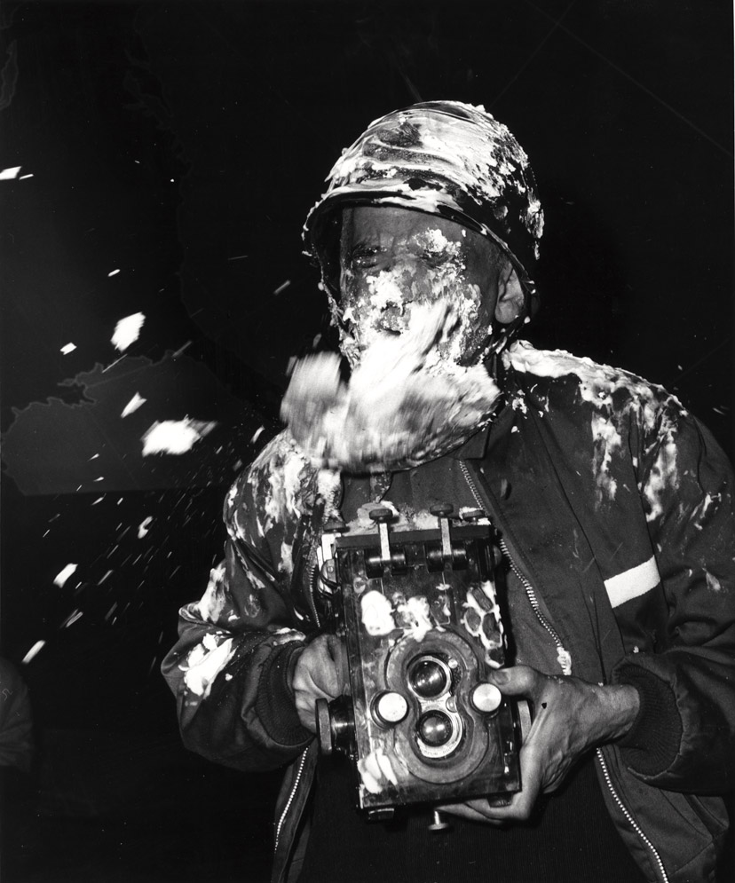 Weegee, with camera, getting hit in the face with a cream pie on the set of Dr. Strangelove, ca.1963