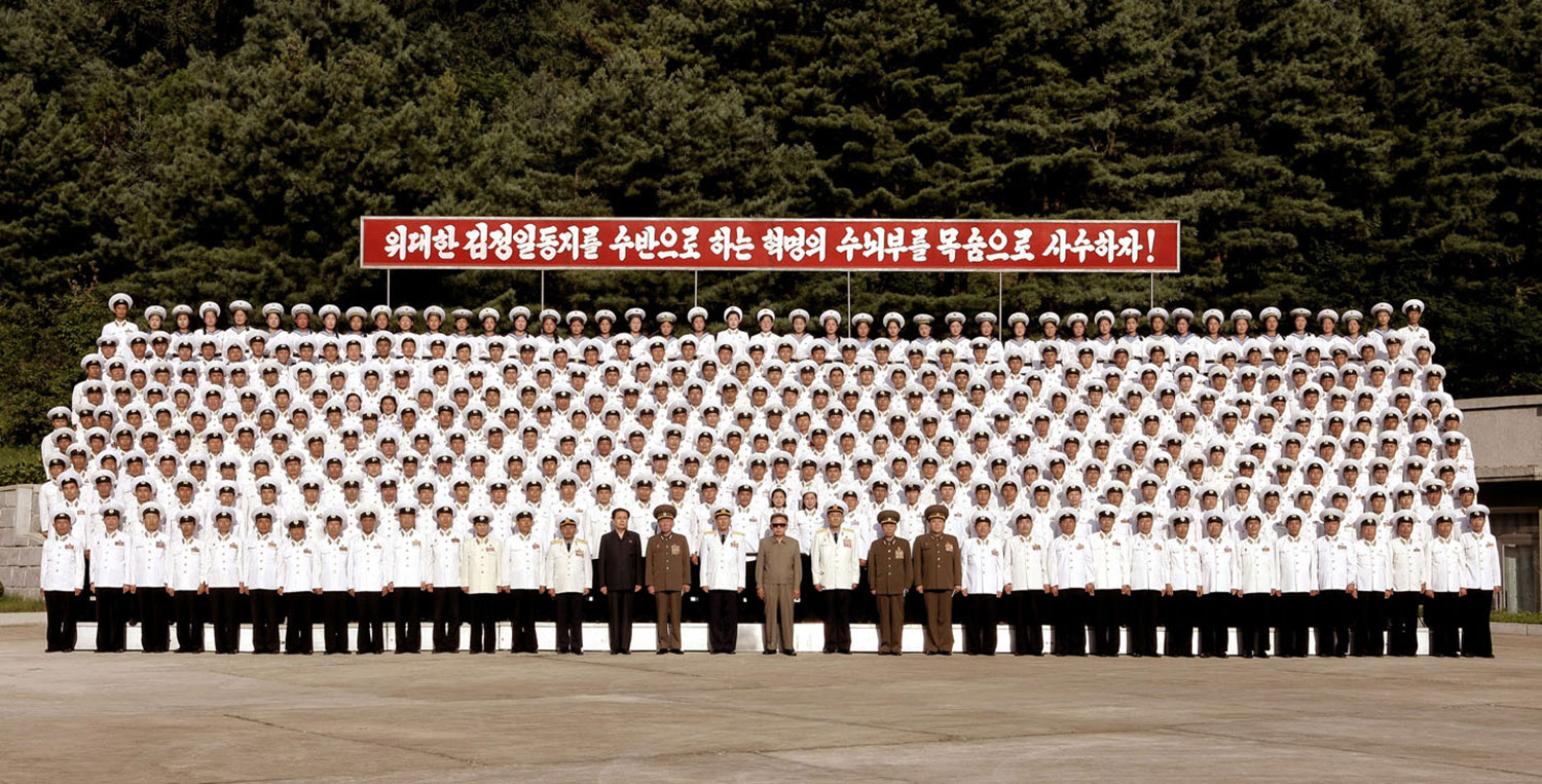 This photo, released by KCNA on July 17, 2009, shows Kim Jong Il (center, in sunglasses), posing with naval officers and soldiers in an undisclosed location.