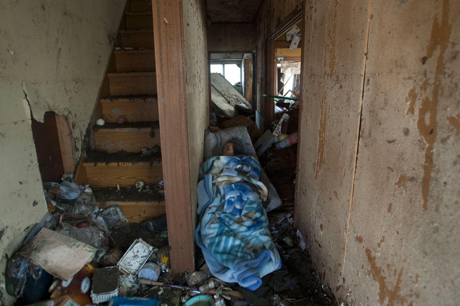 The body of an elderly woman lies next to the stairs in her home in Sendai, Miyagi prefecture, northeastern Japan, on March 13, 2011, two days after the earthquake and tsunami struck the country.