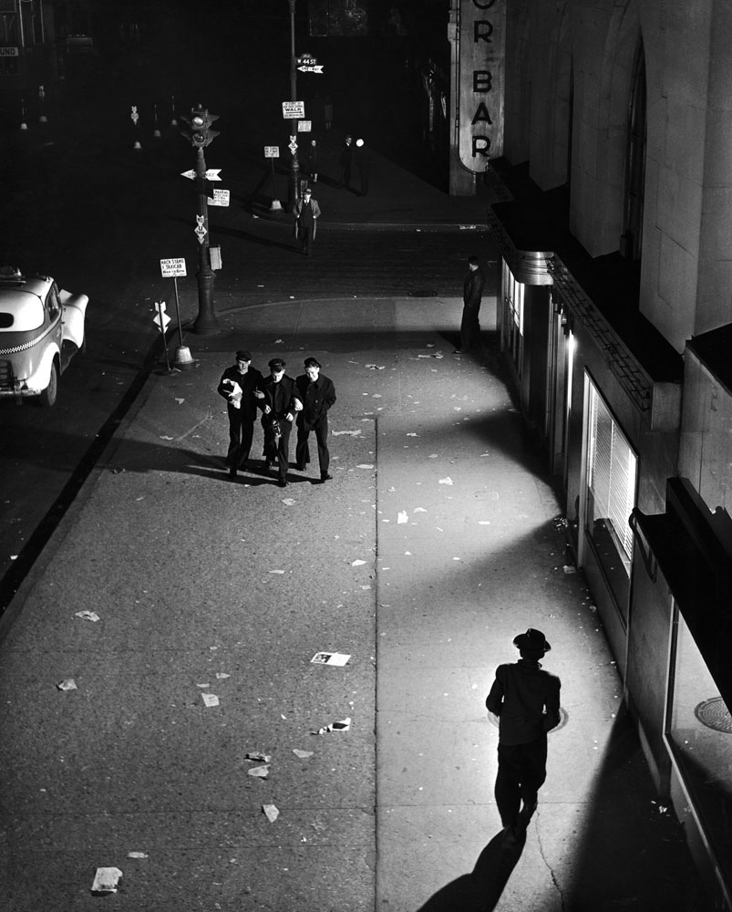 A trio of sailors walk arm in arm down a dimly lit street near Times Square, searching vainly for fun in the curfew-quiet city, February 1945.