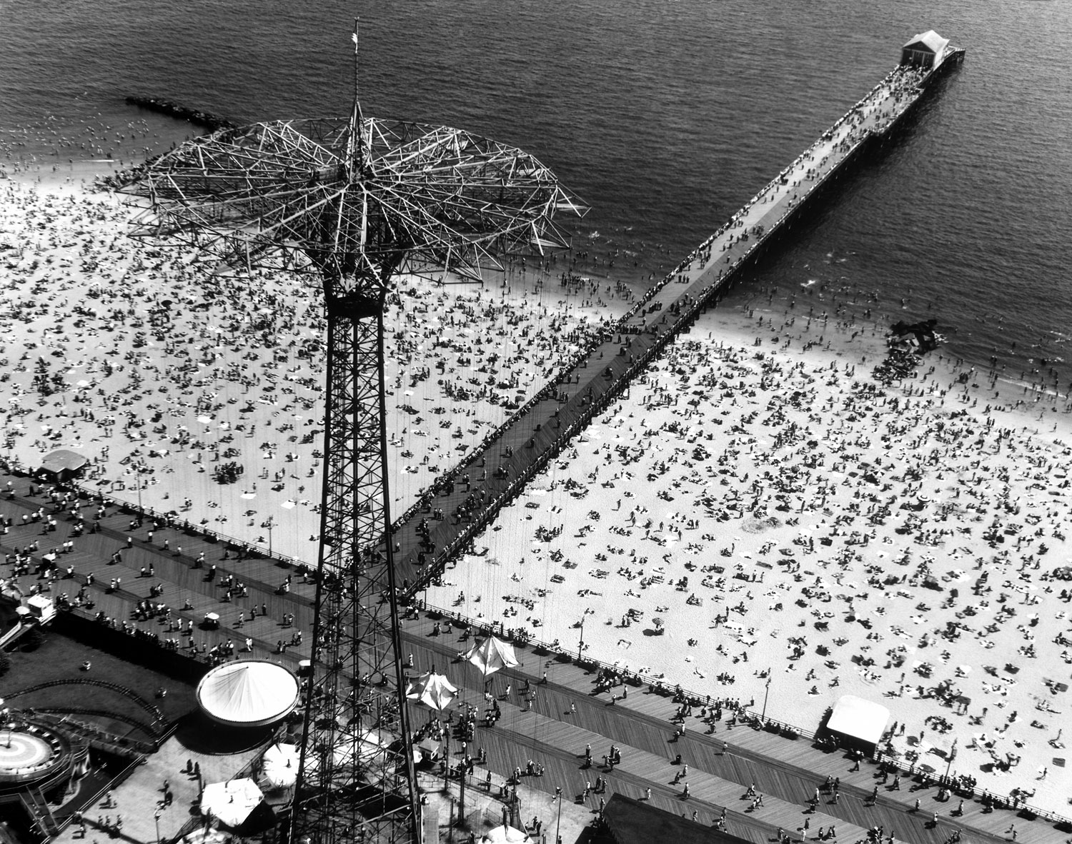 Aerial view of the crowded beach and pier at Coney Island, including the Parachute Jump amusement park ride (the tall structure at left) in Brooklyn, New York, 1951.