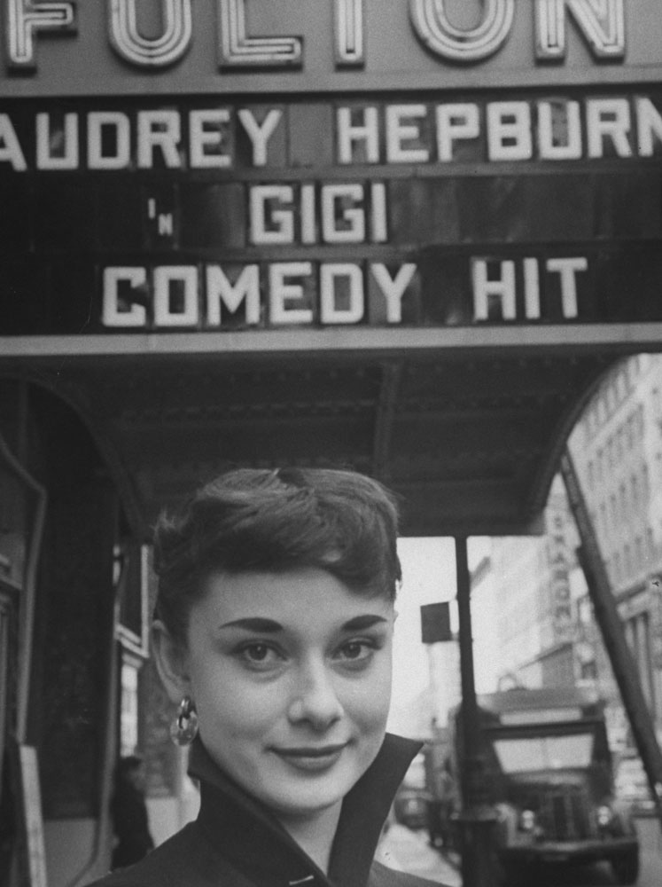 Audrey Hepburn in 1951 — two years before her film breakthrough in Roman Holiday — posing under a theater marquee for the stage version of Gigi.
