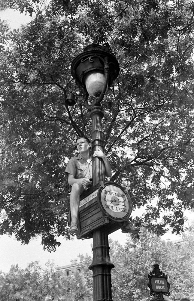 A young man watches liberation celebrations from atop a Parisian light pole in August 1944.