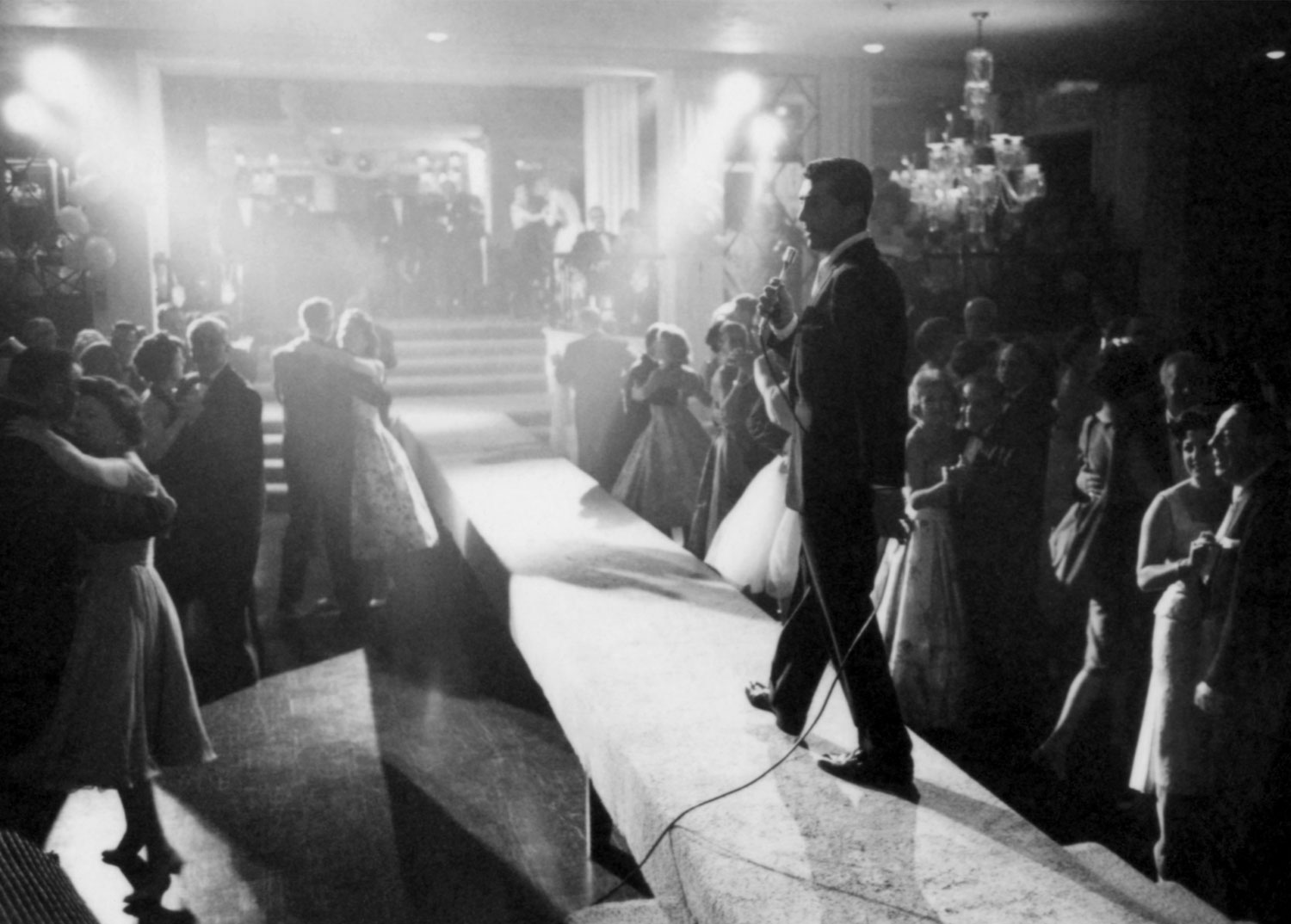 Dean Martin entertains on a narrow stage with couples dancing around him in 1958.