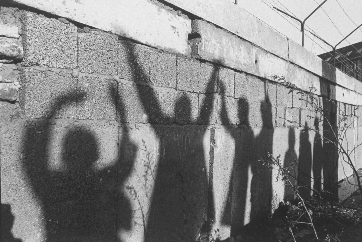 Silhouettes of West Berliners waving to their relatives on the other side are cast across the Berlin Wall.