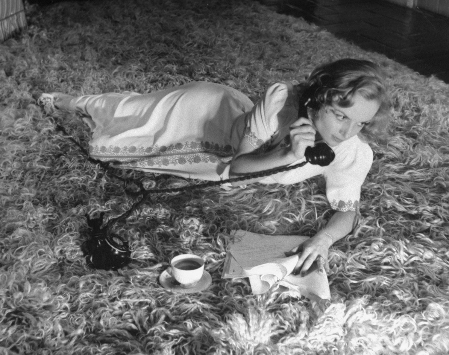 Carole Lombard drinks a cup of coffee and talks on the telephone while lounging on the floor of her Hollywood home in October 1939.