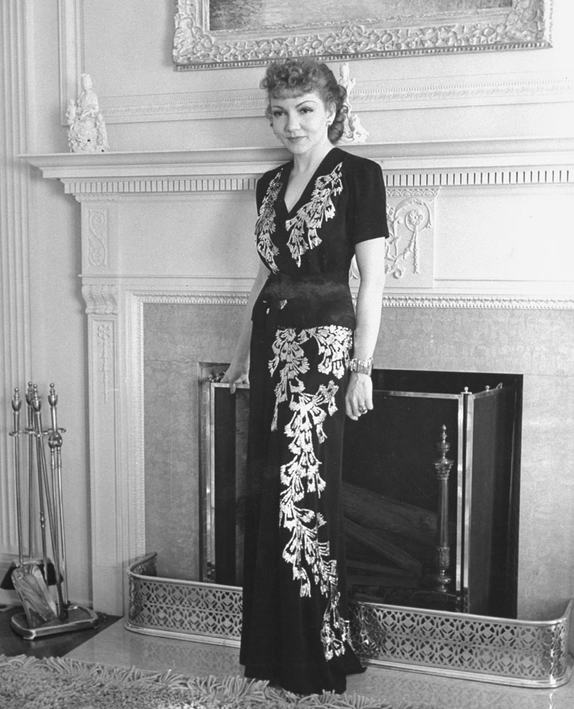 Oscar-winning actress Claudette Colbert poses in a two-piece evening dress in front of the fireplace in her home in Los Angeles' posh Holmby Hills neighborhood in 1939.