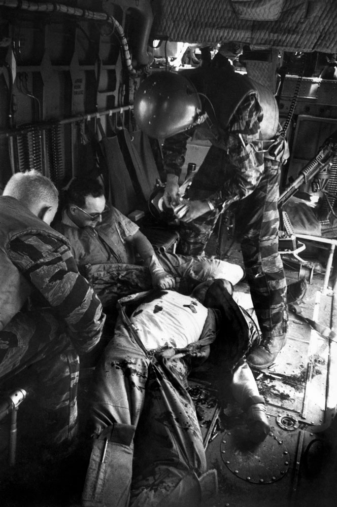 Caption from LIFE.  Farley opens a first-aid kit to apply to Magel's wound as Hoilien watches Owens, the wounded gunner (with dark glasses), slumped in the rear.
