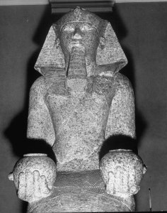 An Egyptian sculpture of a bearded figure kneels while holding objects in both hands in the Collection of the Metropolitan Museum of Art.