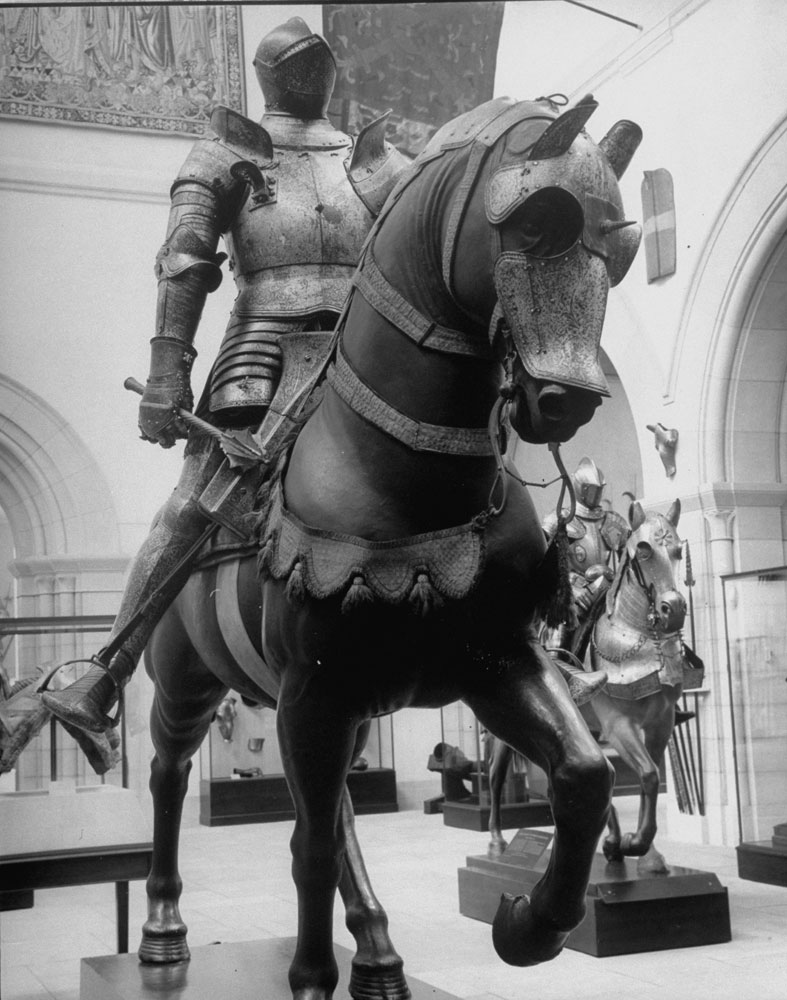A fully armored figure sits atop a partially armored horse figure in the Hall of Armor at the Metropolitan Museum of Art.