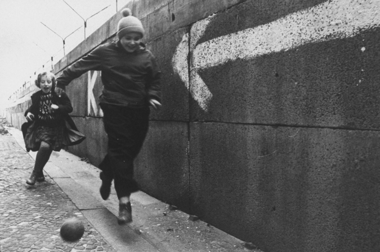 Children chase a ball beside the Berlin Wall