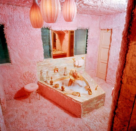 Jayne Mansfield combs her hair while bathing in the pink carpeted bathroom of her home, known as 