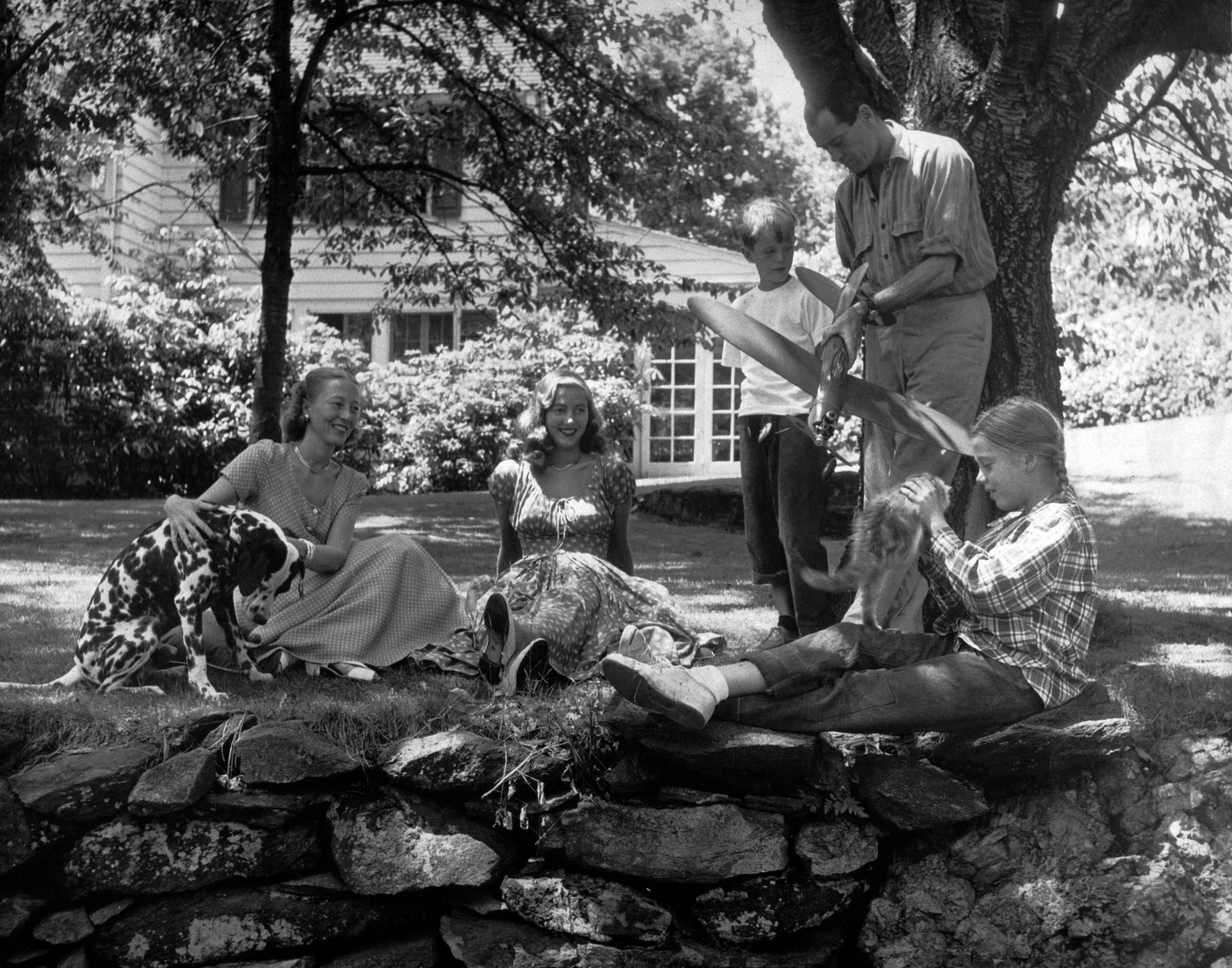 Henry Fonda shows a toy plane to son Peter Fonda while daughter Jane Fonda plays with cat, stepdaughter Frances Brokaw and wife Frances watches in yard at home in Connecticut in 1948