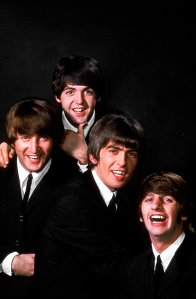 John Lennon, Paul McCartney, George Harrison, and Ringo Starr pose in a portrait on a black backdrop in January 1964