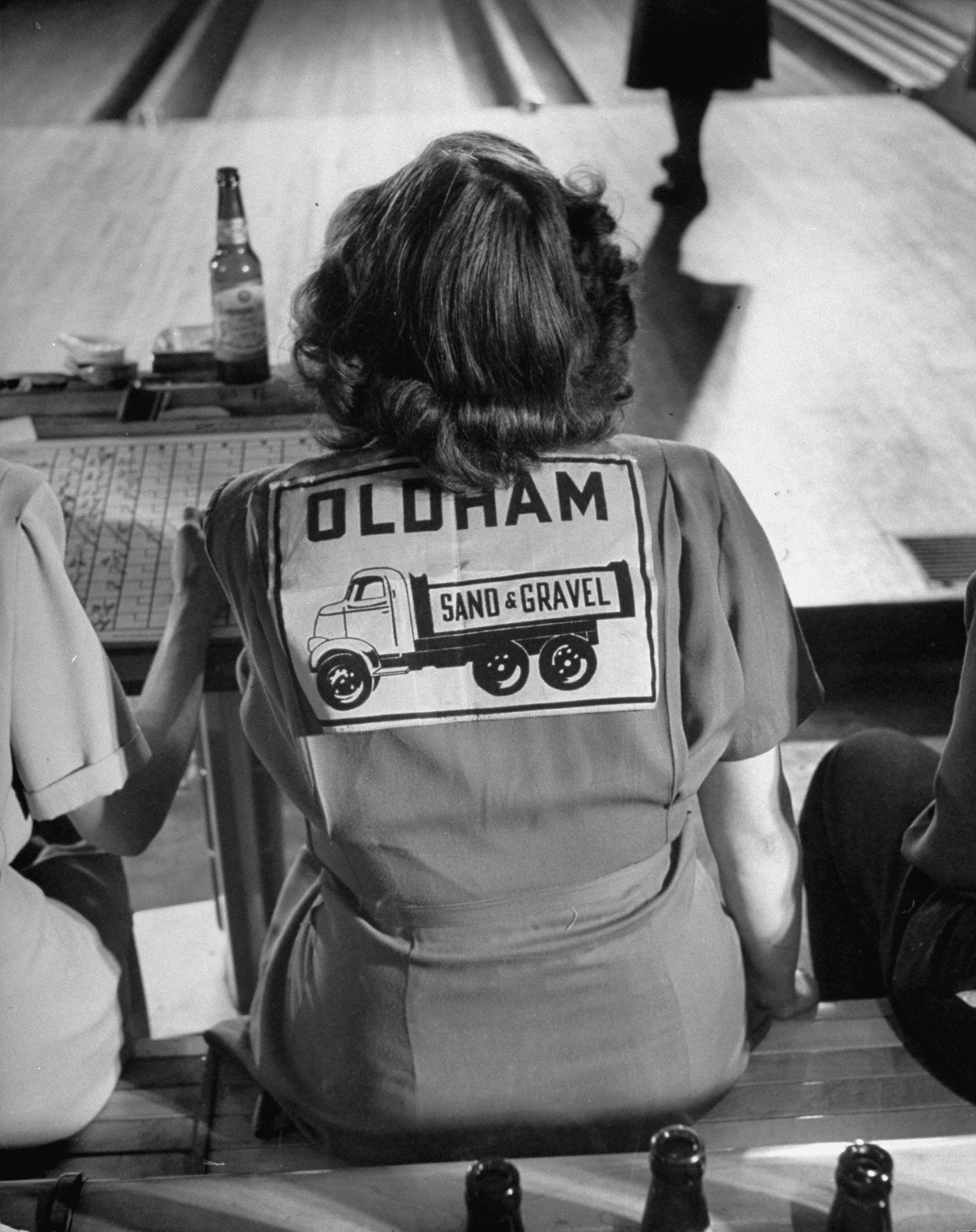 A female bowling team member wears a shirt representing her team and sponsor.