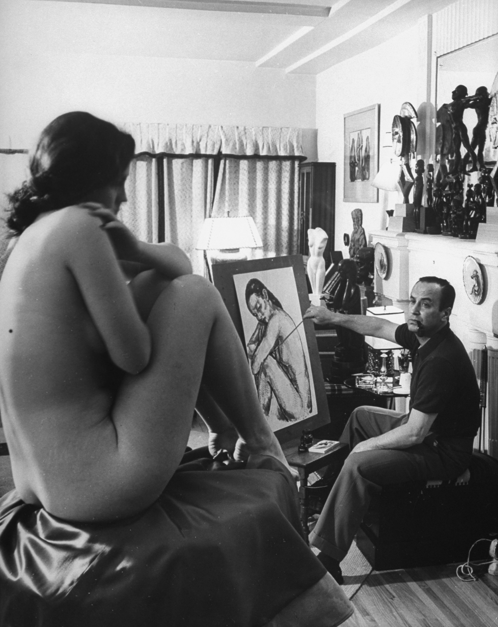 Jean Negulesco (1900 - 1993) paints a portrait of a nude model in his Hollywood studio.