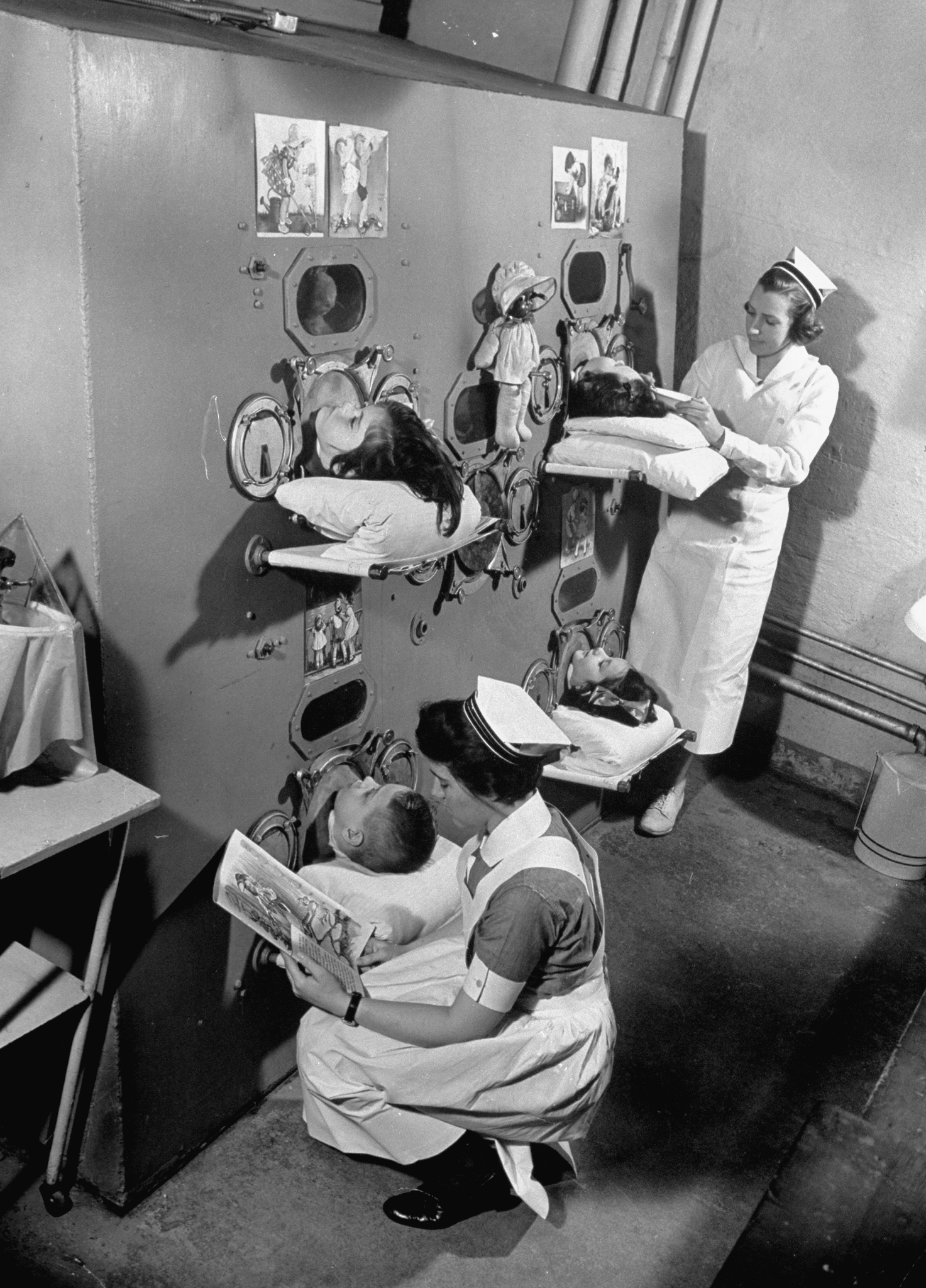 Nurses tend to four young polio patients lying on beds inside an "iron lung" in 1938.