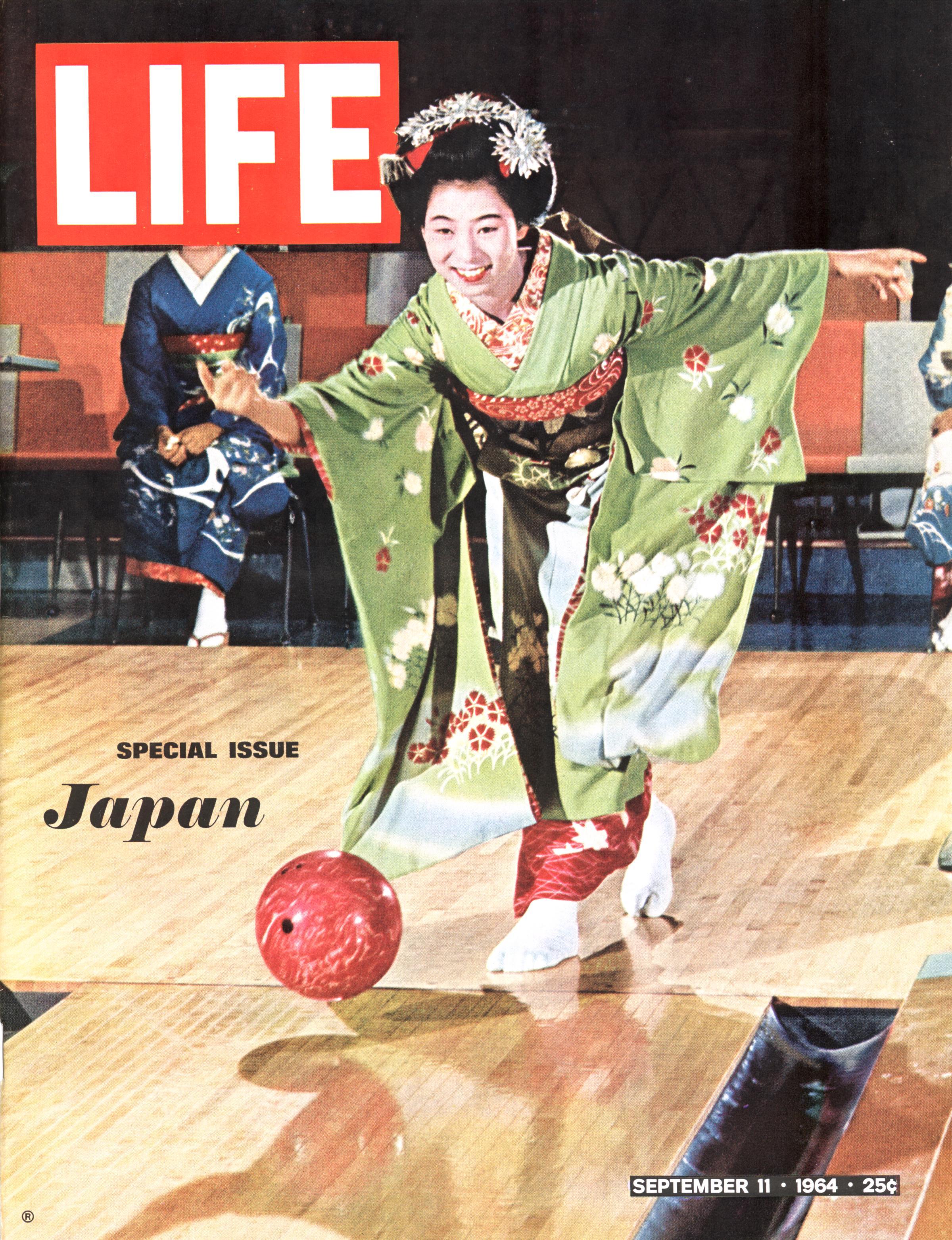An apprentice geisha in a kimono and full make-up smiles as she bowls on a lane, watched by several other geisha in Kyoto, Japan.