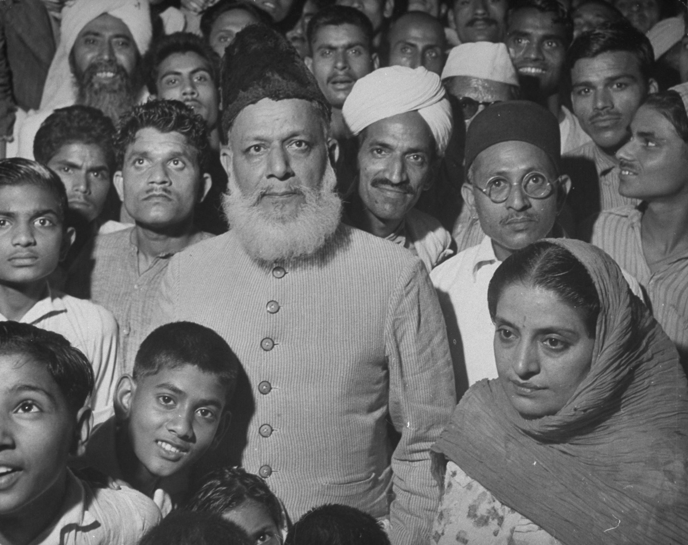 Hindu men and women crowd around gray-bearded Anis Ahmed, a Muslim maulana (scholar),
