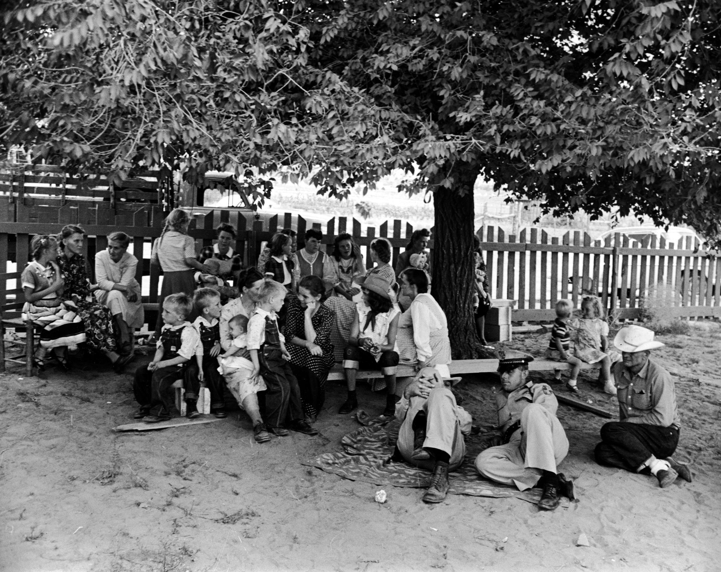 Short Creek raid, Arizona, 1953. As arraignments of the adults drag on in Short Creek's schoolhouse, transformed by the authorities into a temporary site for pre-trial hearings, a group of children and women wait in the schoolyard with state police guarding them.