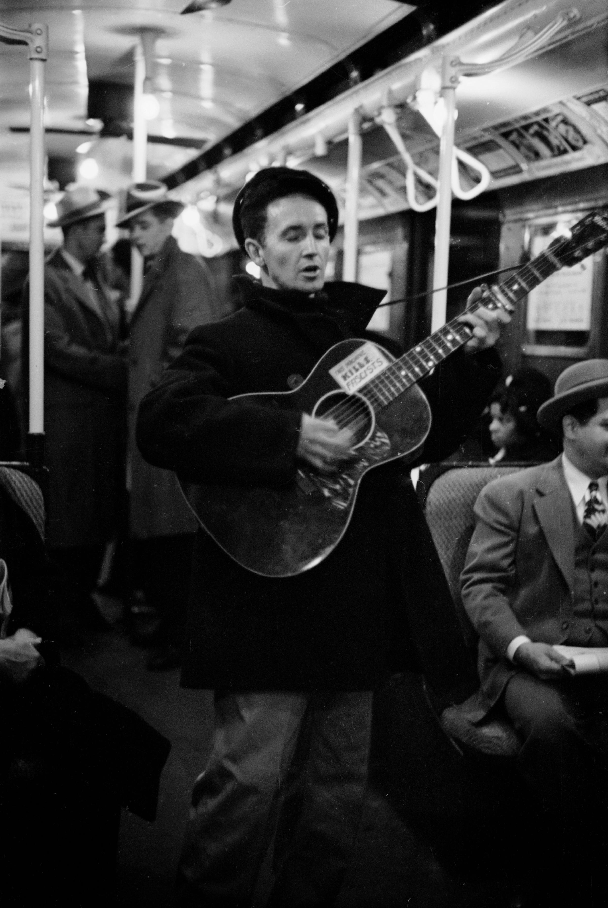 Woody Guthrie entertains New York commuters in 1943, strumming a guitar bearing his now-famous slogan, "This Machine Kills Fascists."