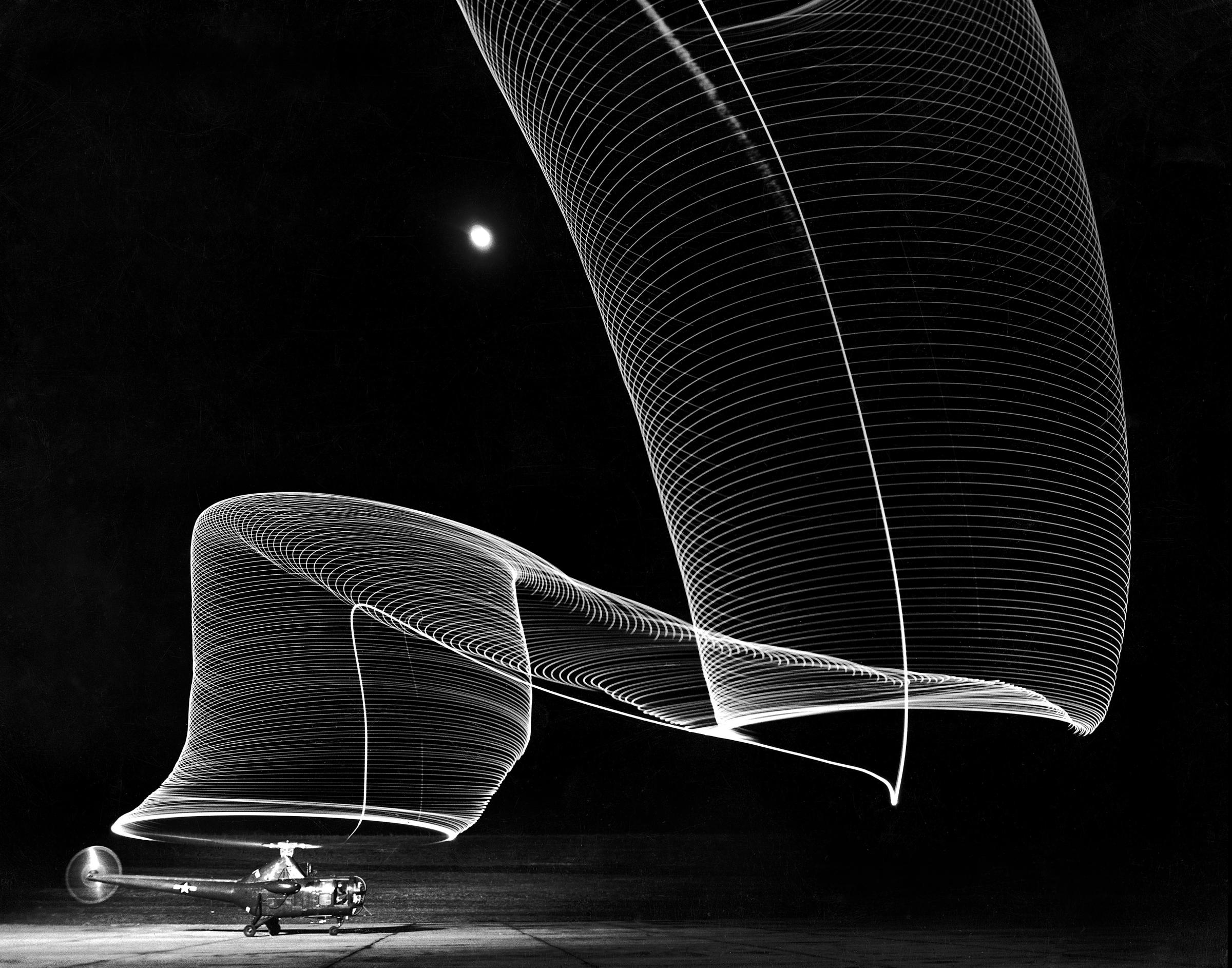 A long exposure view of a Sikorsky S-51 helicopter on the ground at Anacostia Naval Air Station in Washington, DC in 1949. The striking "Slinky shape" is produced by light reflecting on the rotor blades and leaving a trail in the night sky.