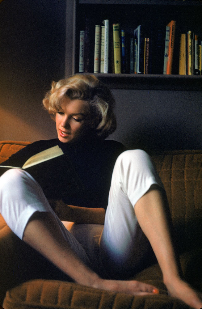 Marilyn Monroe Reads at Home. She is wearing a black shirt and white capri pants in 1953.