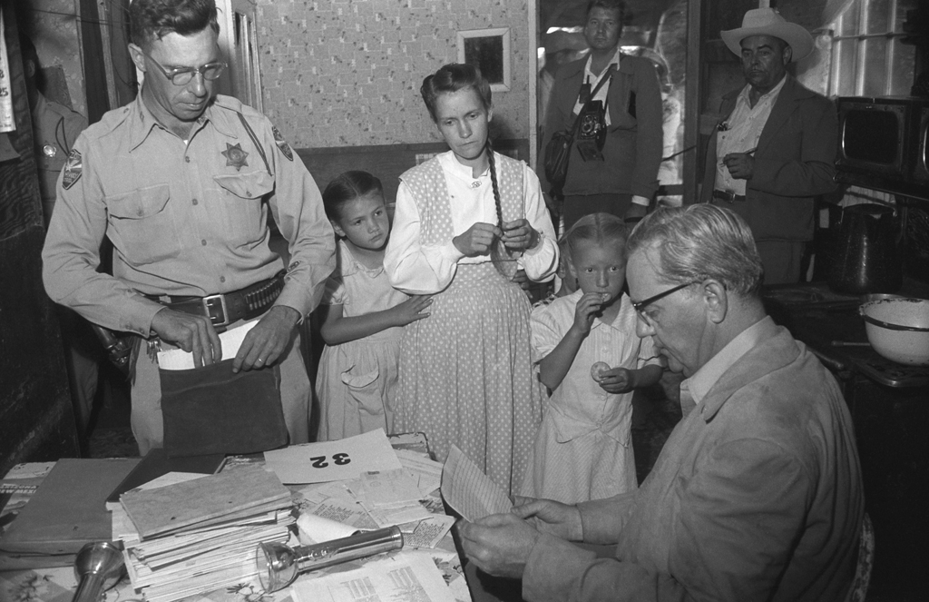 Two girls stand with their mother as she is questioned by an officer and Arizona Attorney General Ross Jones after the 1953 Short Creek raid.