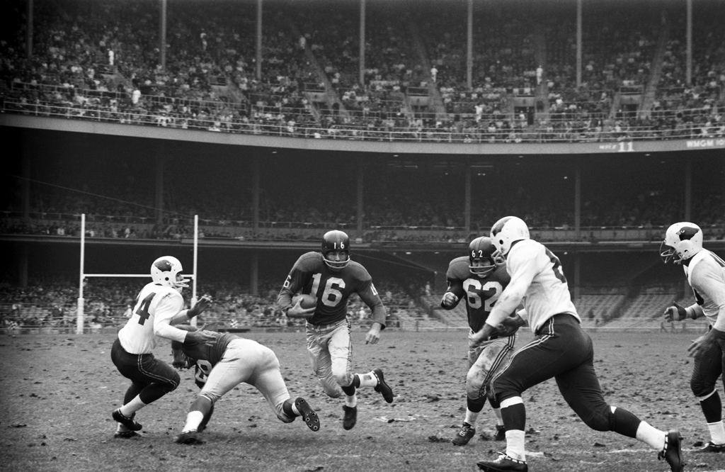 Frank Gifford carries the ball against the Cardinals as guard Darrell Dess (#62) runs interference.